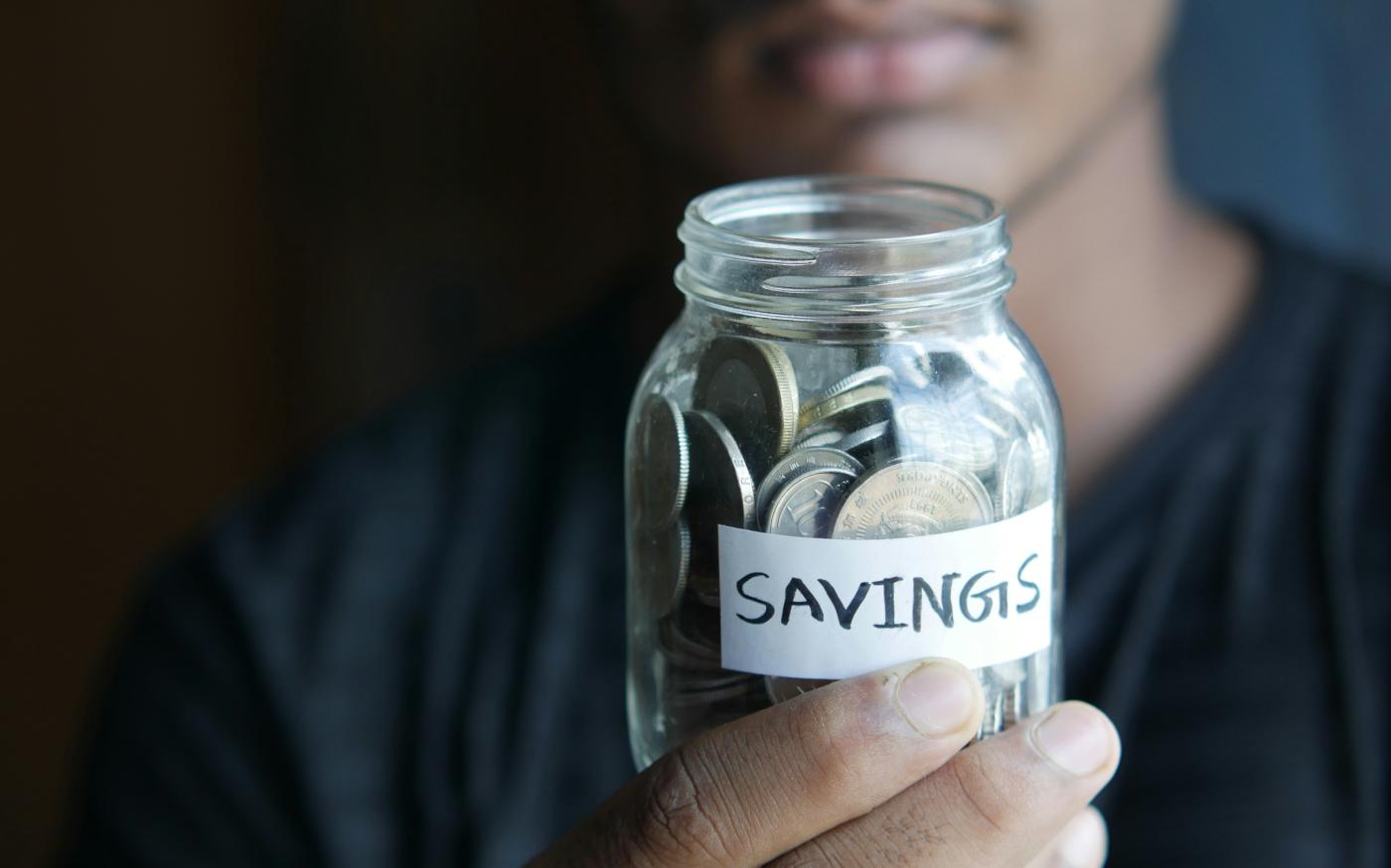 a man holding a jar with a savings label on it by Towfiqu barbhuiya courtesy of Unsplash.